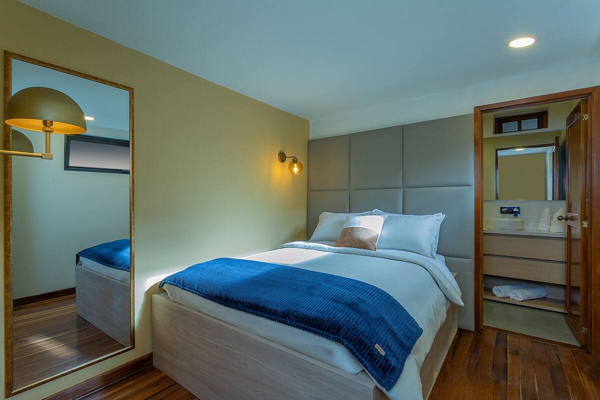 Een hotelkamer met een bed, een grote spiegel, een nachtkastje, een wandlamp en een ingebouwd schap met handdoeken.