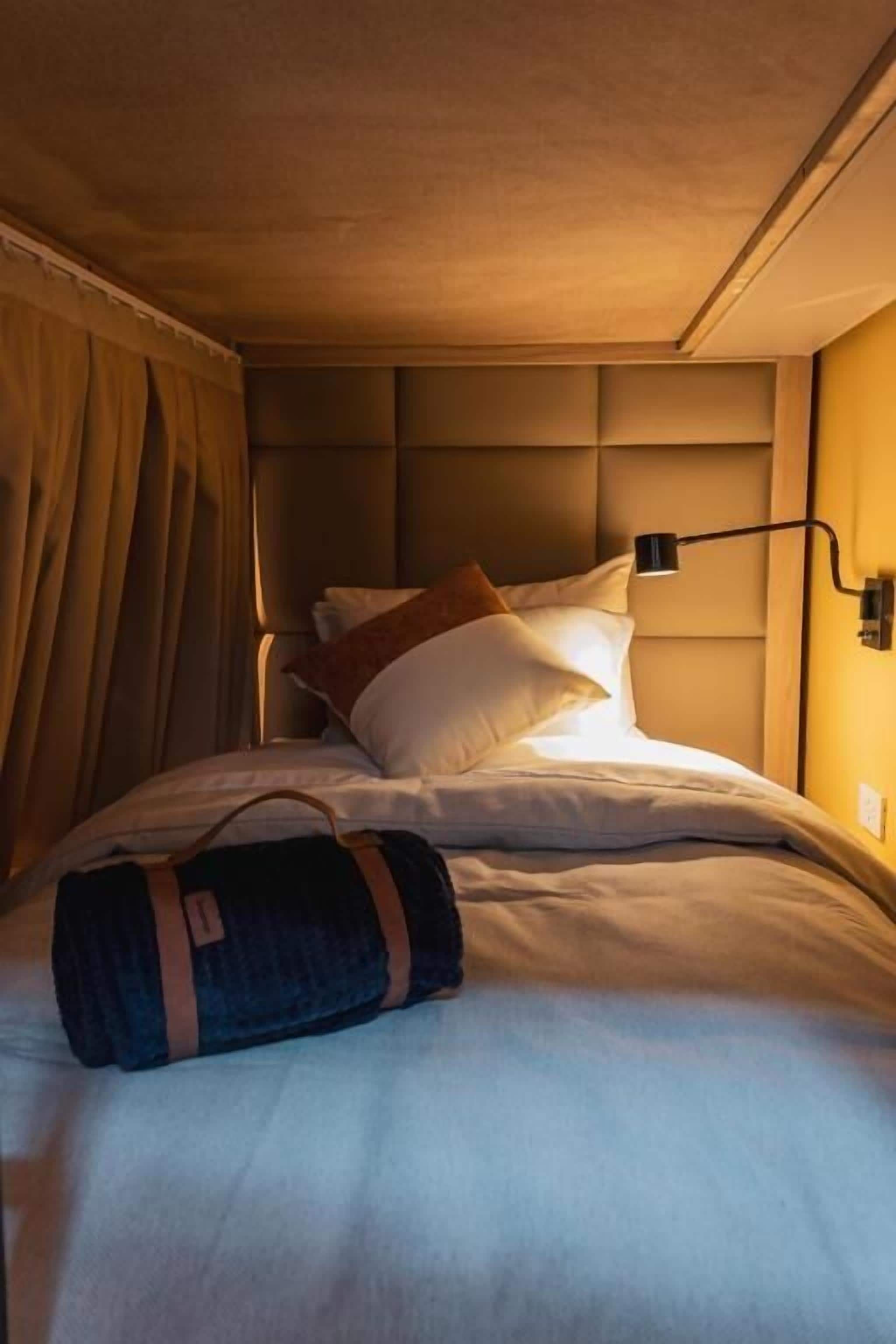 A hotel room with a bed, a headboard, a lamp, and a suitcase.