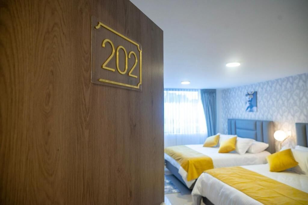 Habitación de hotel con dos camas, una pared de madera con un cartel de número y una ventana con cortinas.