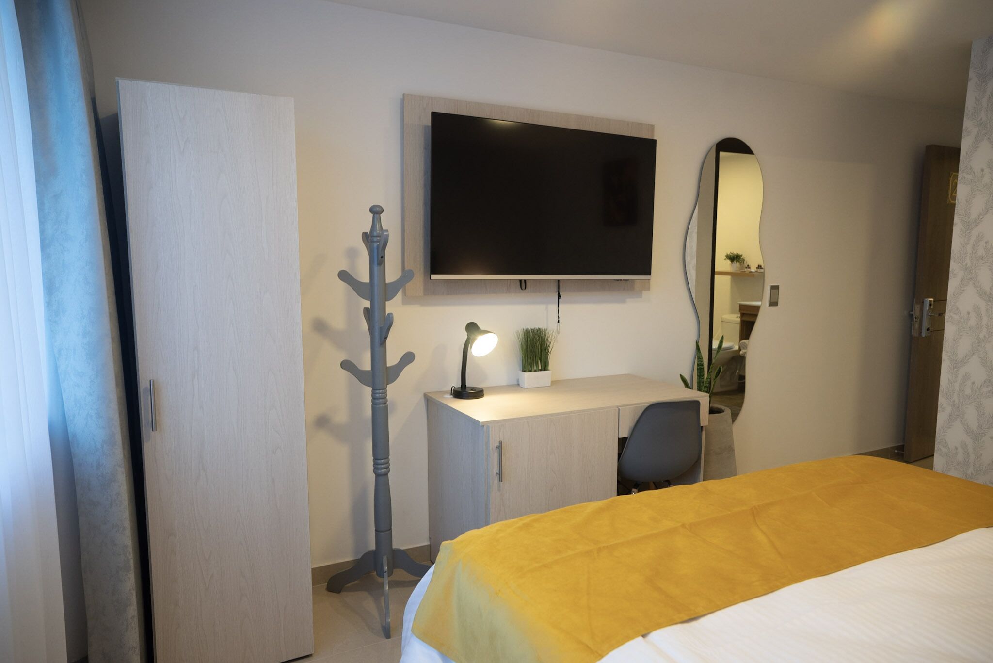 A hotel room with a bed, a desk, a chair, a TV, a wardrobe, and a mirror.