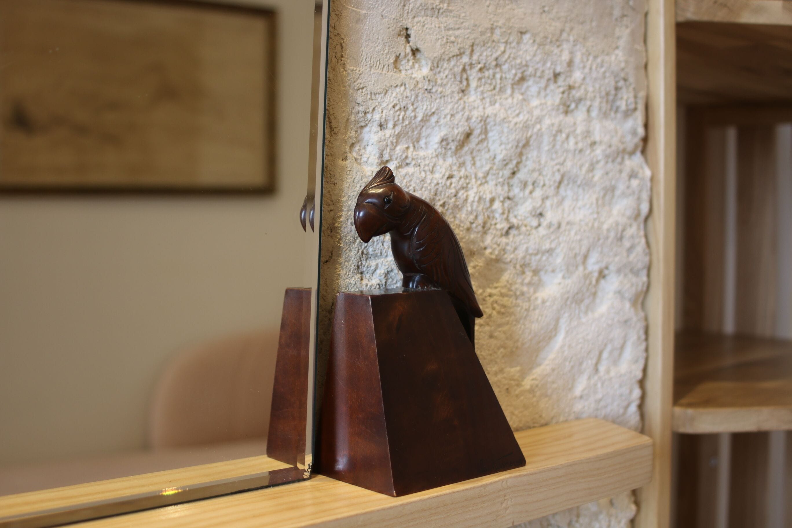 A wooden shelf with a dark brown sculpture of a cat on a pedestal against a textured wall.