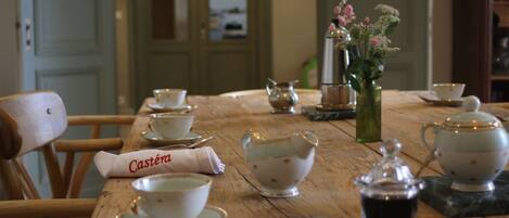 A wooden dining table with tea cups, saucers, a teapot, and a sugar bowl.