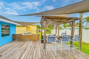 A wooden deck with a barbecue area, outdoor seating, and a pergola providing shade. - Pet-Friendly Fort Pierce Home w/ Pool & Game Room! (Fort Pierce)
