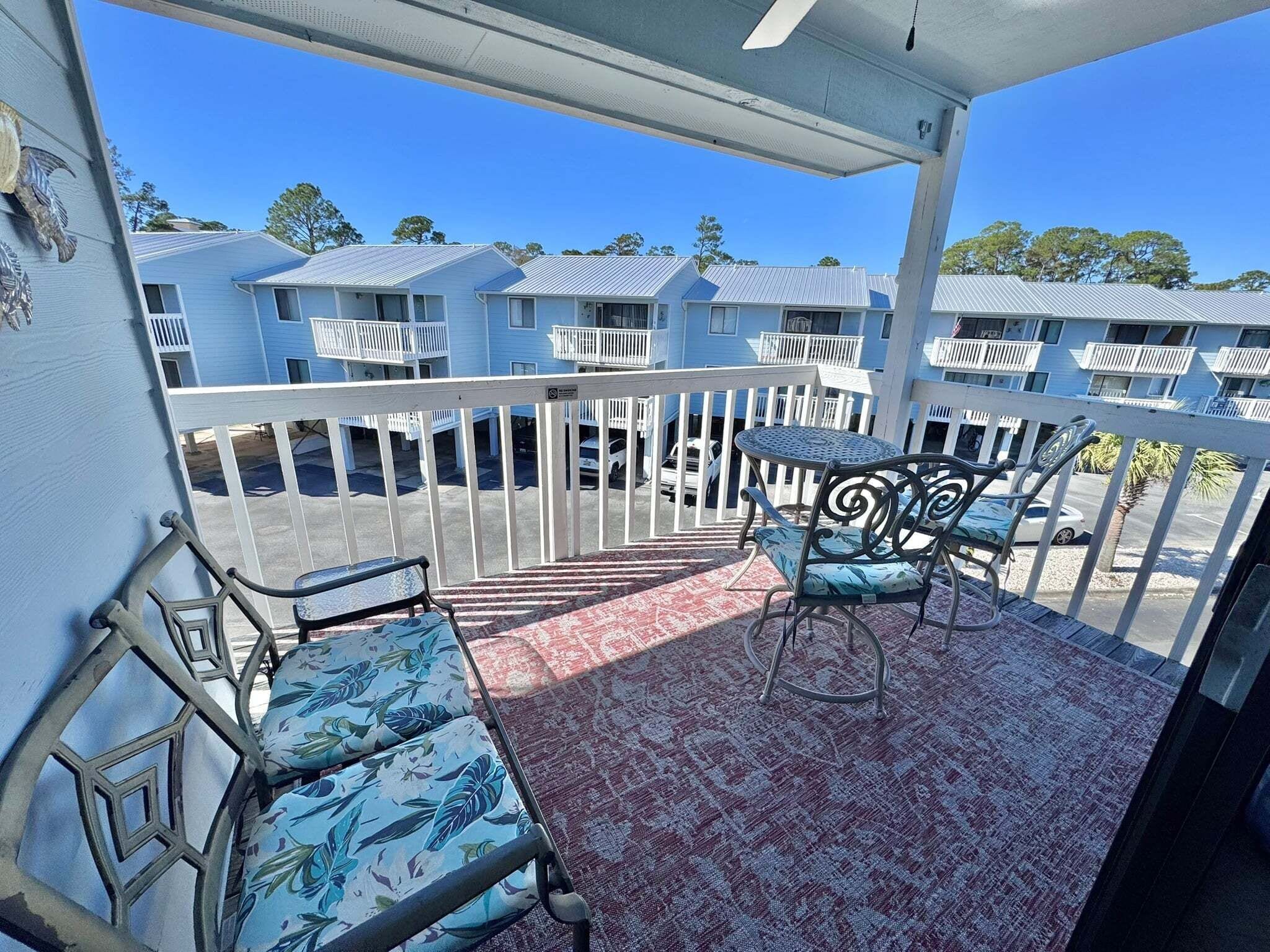 A balcony with a patterned rug, metal chairs, and a small table.