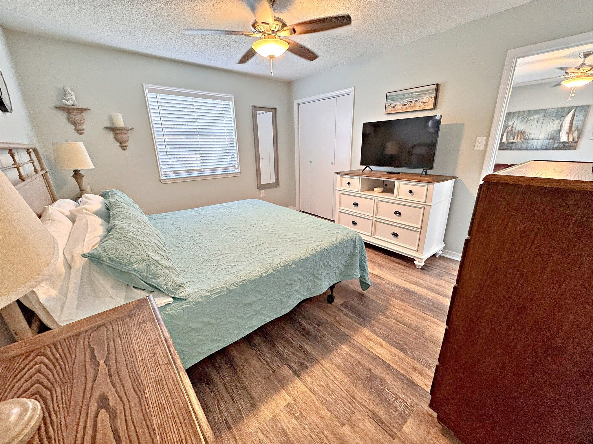 A bedroom with a bed, dresser, television, and ceiling fan.