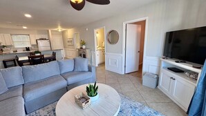 A modern living room with a grey sectional sofa, a round coffee table with a plant, a TV on a stand, and a ceiling fan. - Bayview (Orange Beach)