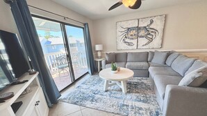 A living room with a grey sofa, a coffee table, a TV, and a large window with curtains. - Bayview (Orange Beach)