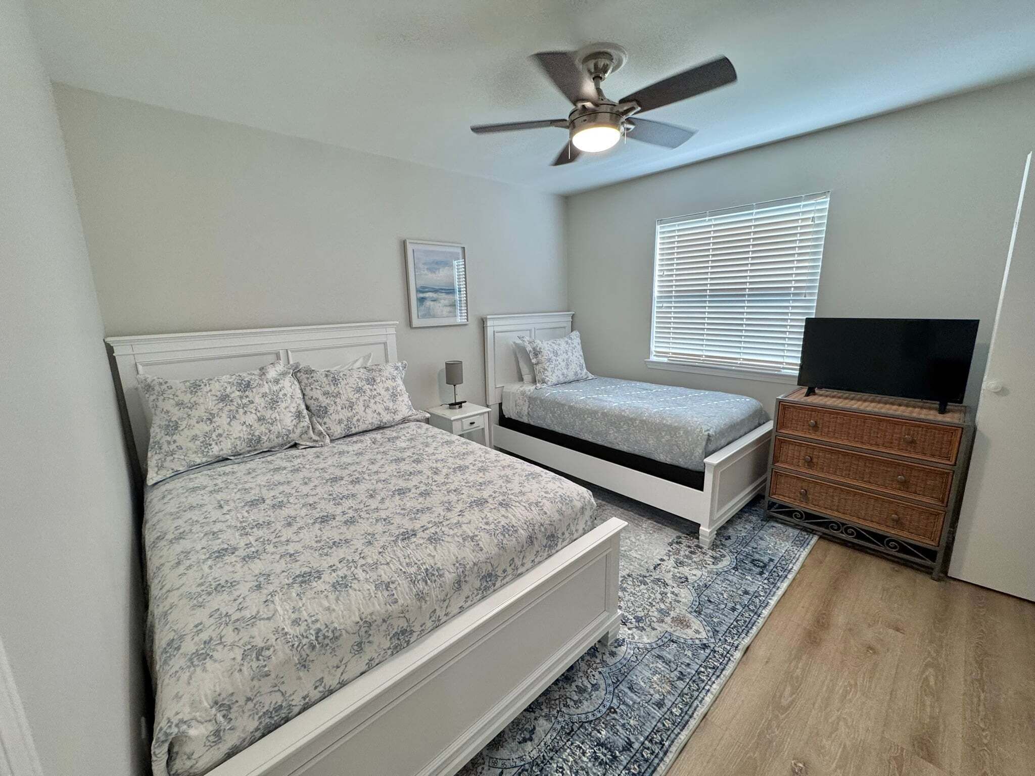 A bedroom with a bed, bedside tables, a ceiling fan, a TV on a dresser, and a window with blinds.