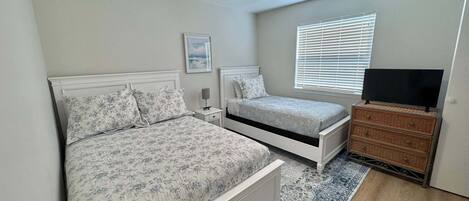 A bedroom with a bed, bedside tables, a ceiling fan, a TV on a dresser, and a window with blinds.