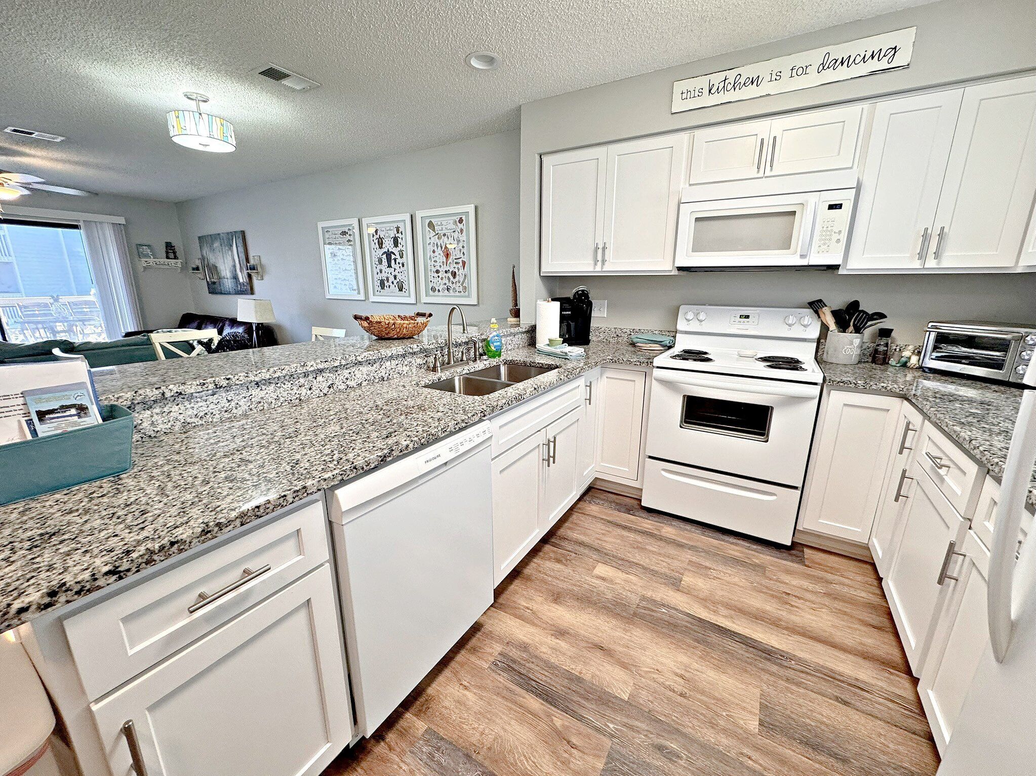 A modern kitchen with white cabinets, granite countertops, a built-in oven, microwave, and toaster.