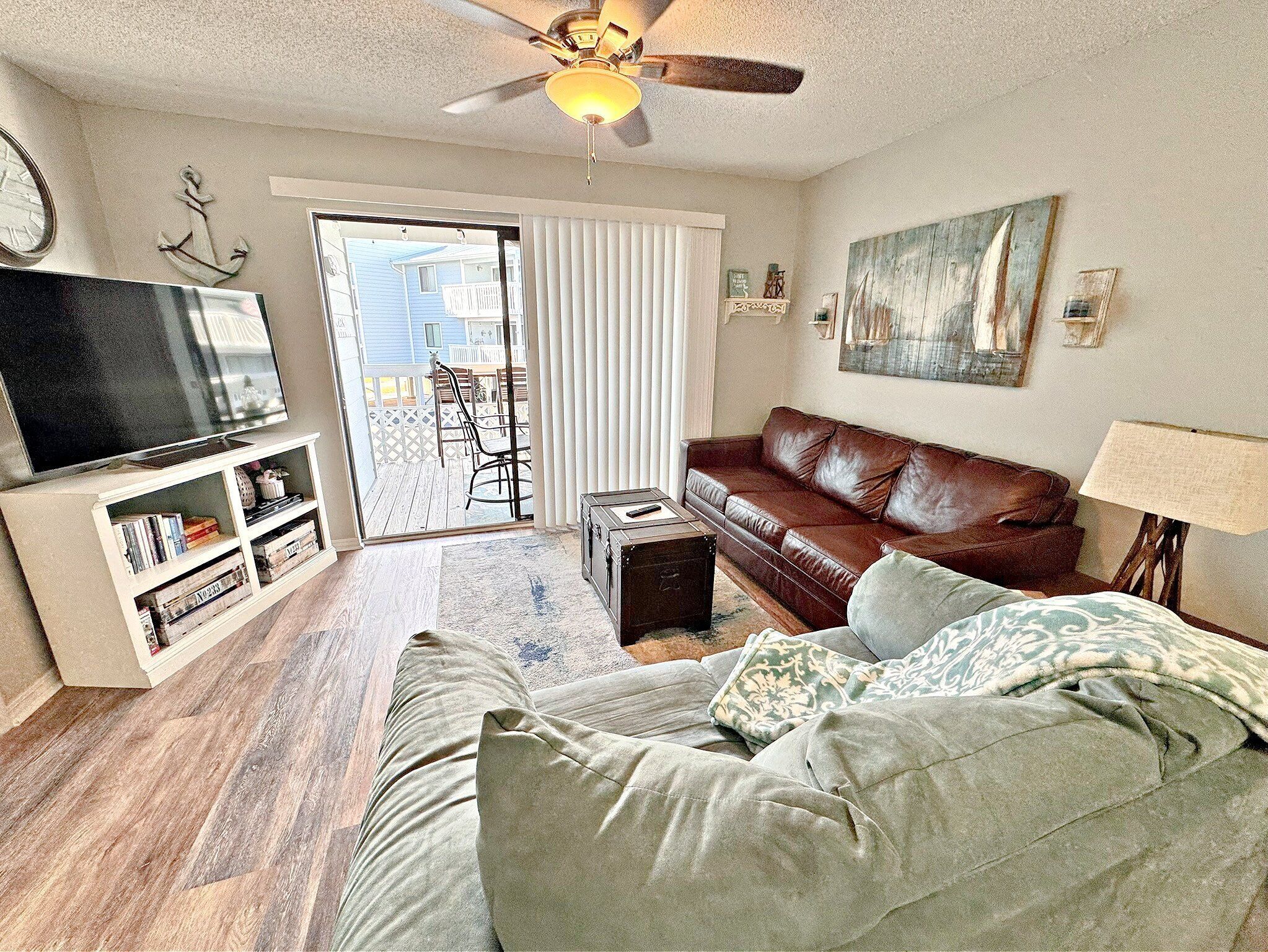 A living room with a brown leather sofa, a television, a bookshelf, and a ceiling fan.