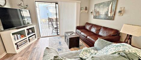 A living room with a brown leather sofa, a television, a bookshelf, and a ceiling fan.