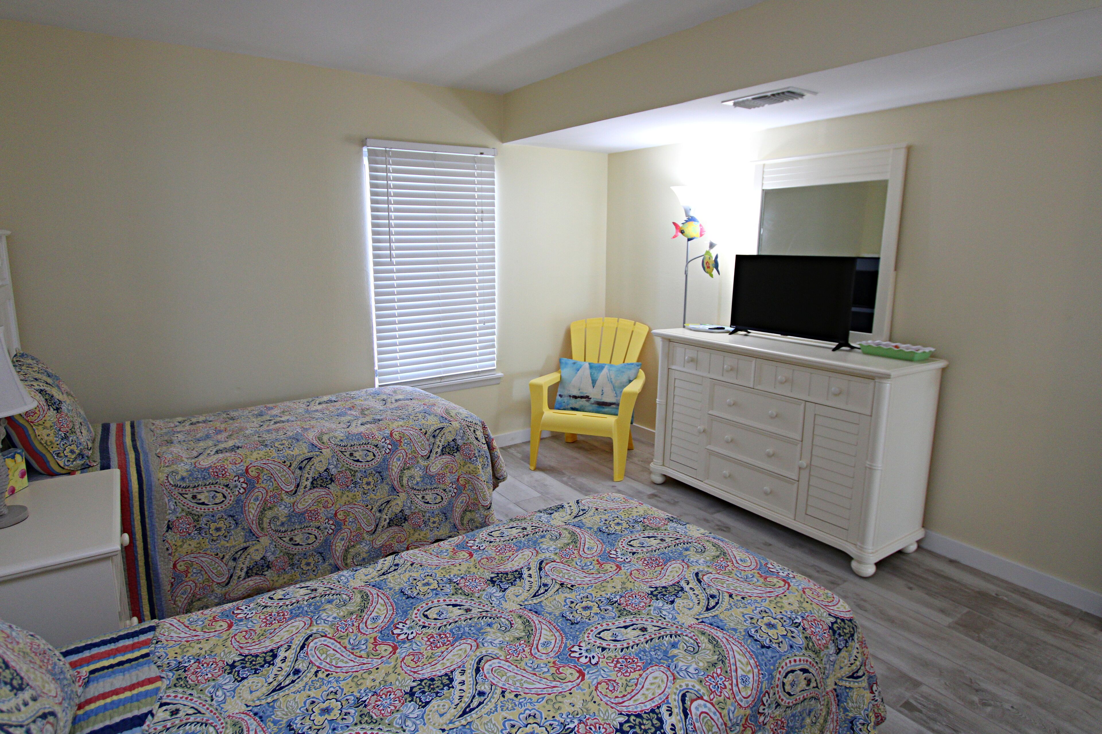 Un dormitorio con dos camas, una silla, un aparador y un televisor.