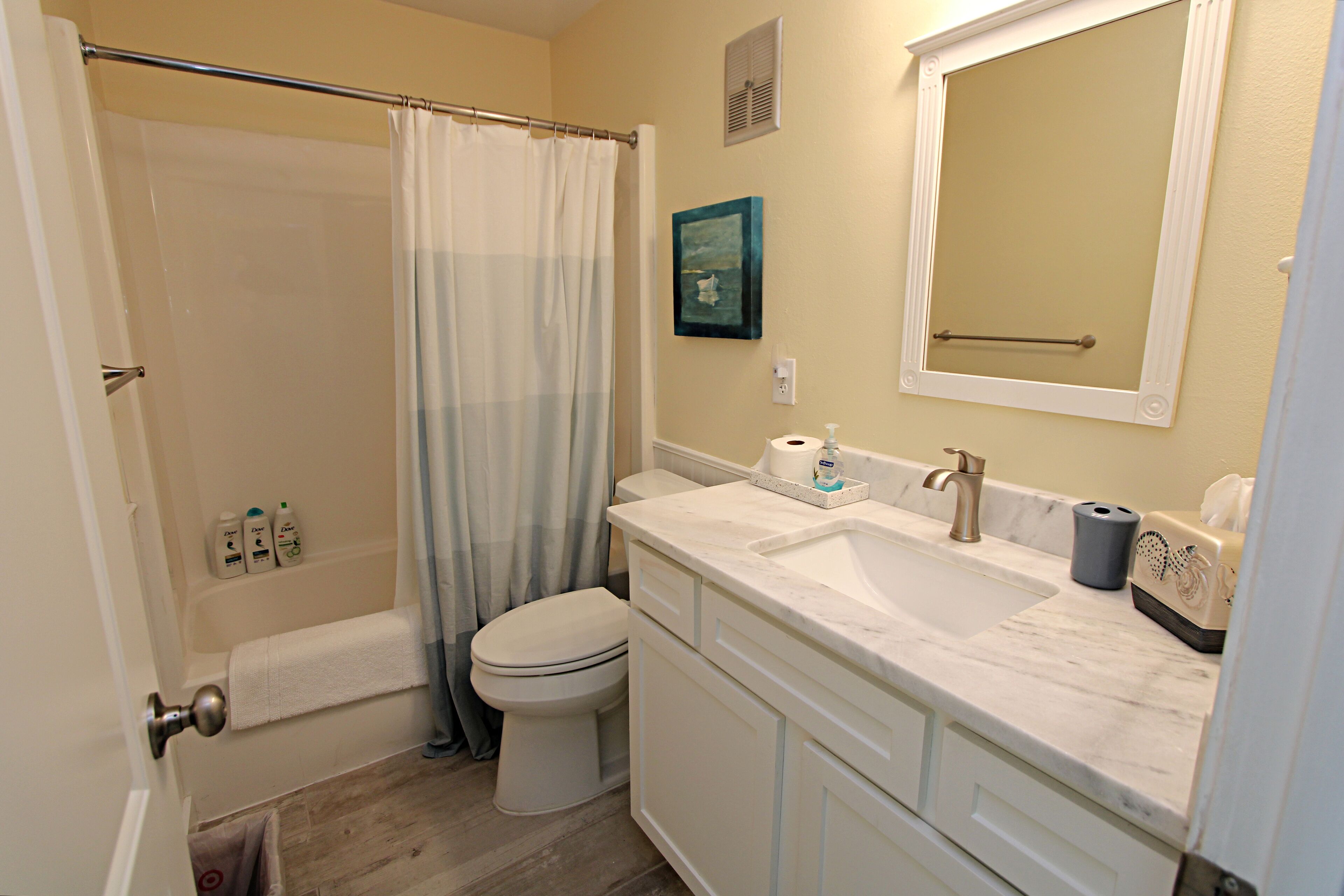 A bathroom with a shower, toilet, sink, and mirror.