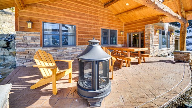 Eine Blockhütte mit Kamin aus Stein, einer Holzterrasse und einer Sitzgelegenheit im Freien.