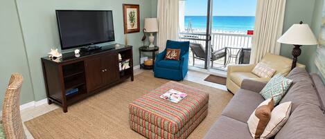 Una sala de estar con televisión, sofá, reposapiés y vista a la playa a través de puertas correderas.