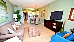 A living room with a sofa, ottoman, and a television. - Caribbean (Gulf Shores)
