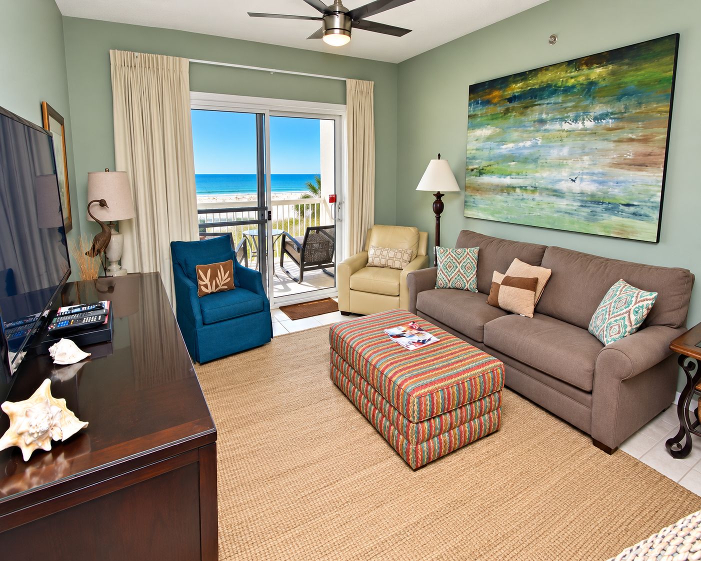A living room with a view of the beach, a ceiling fan, a TV, and a coffee table.