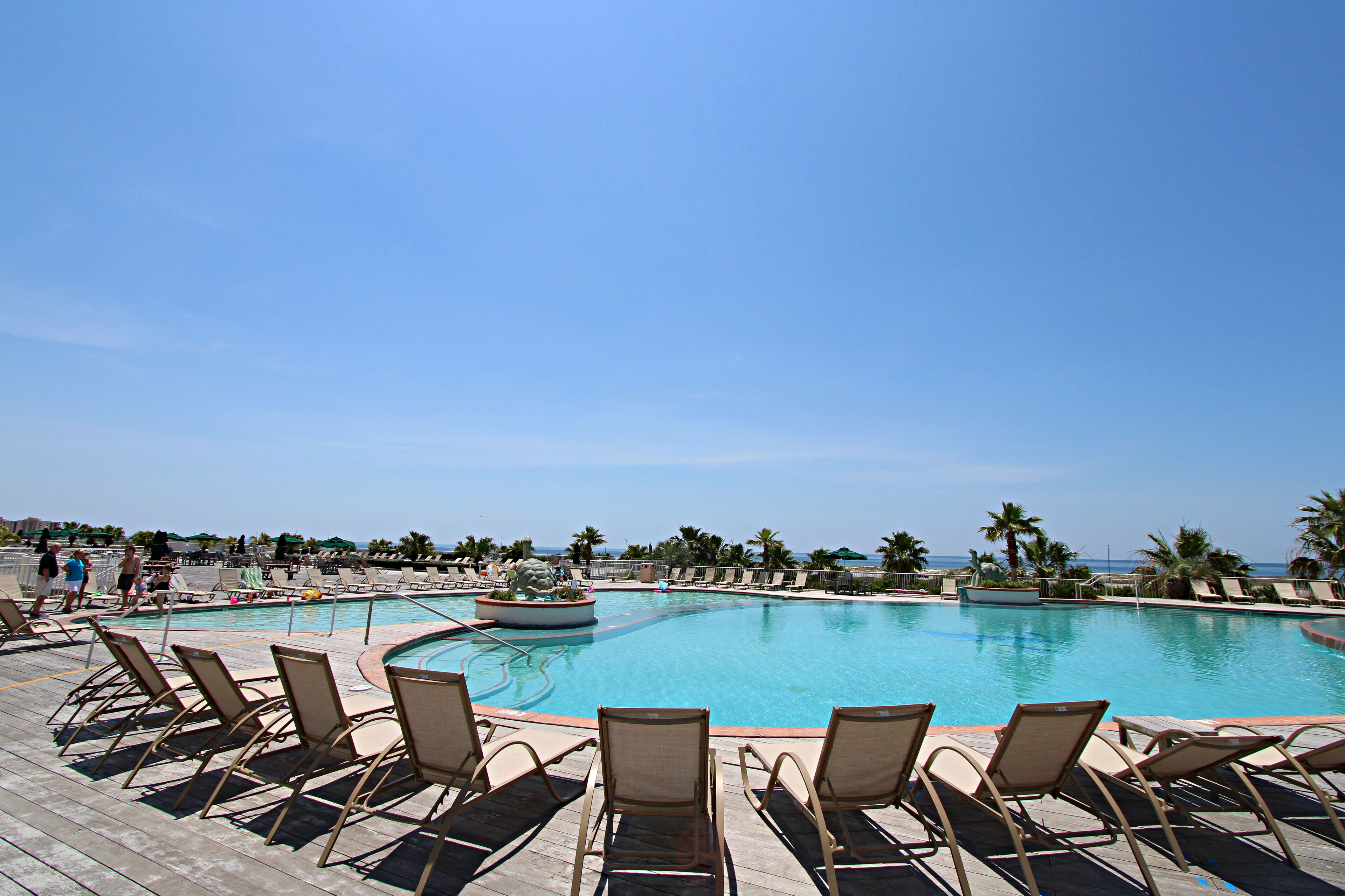 A pool area with lounge chairs and a clear view of the ocean.