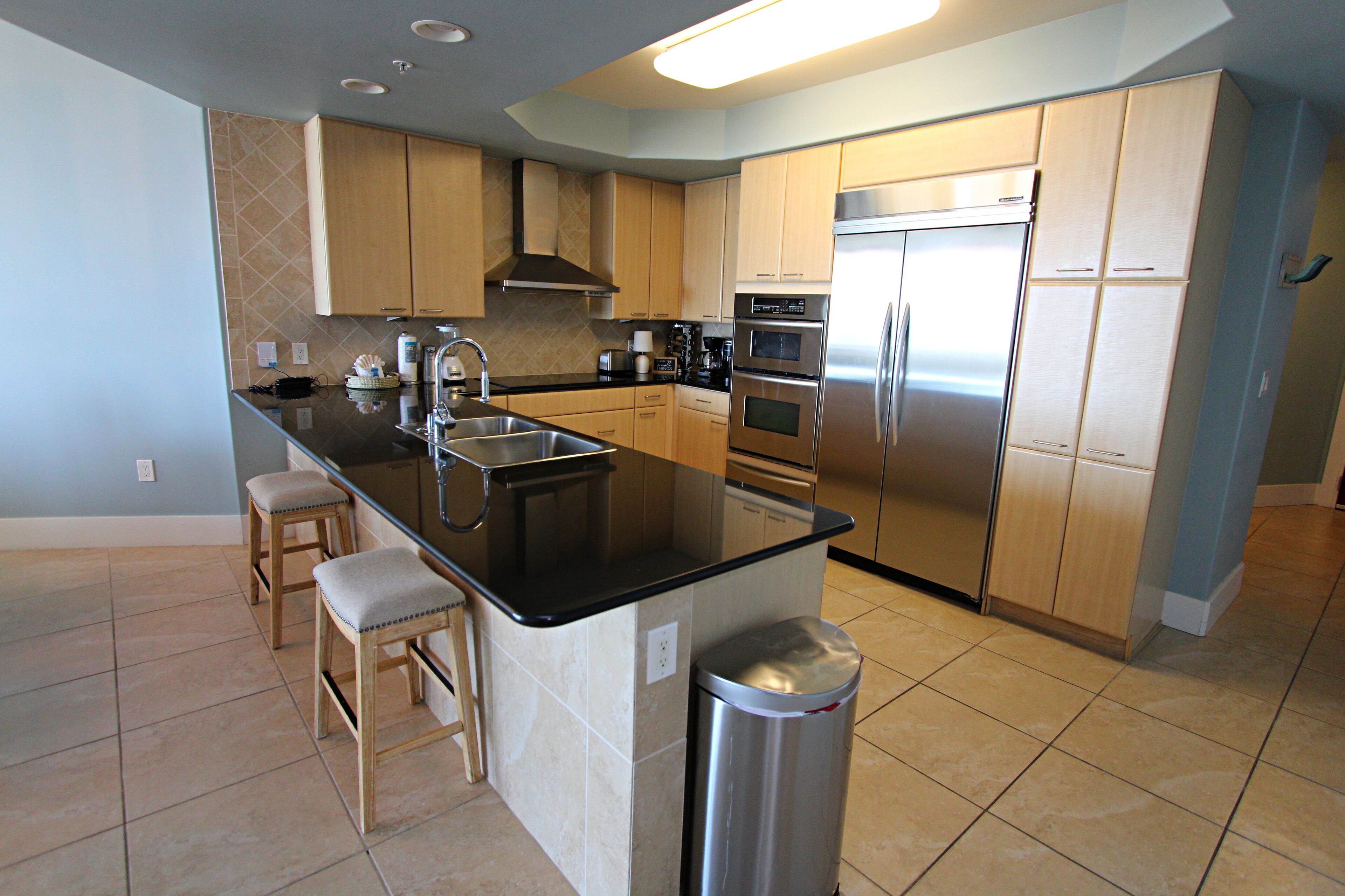 A modern kitchen with a central island, stainless steel appliances, and light wood cabinets.