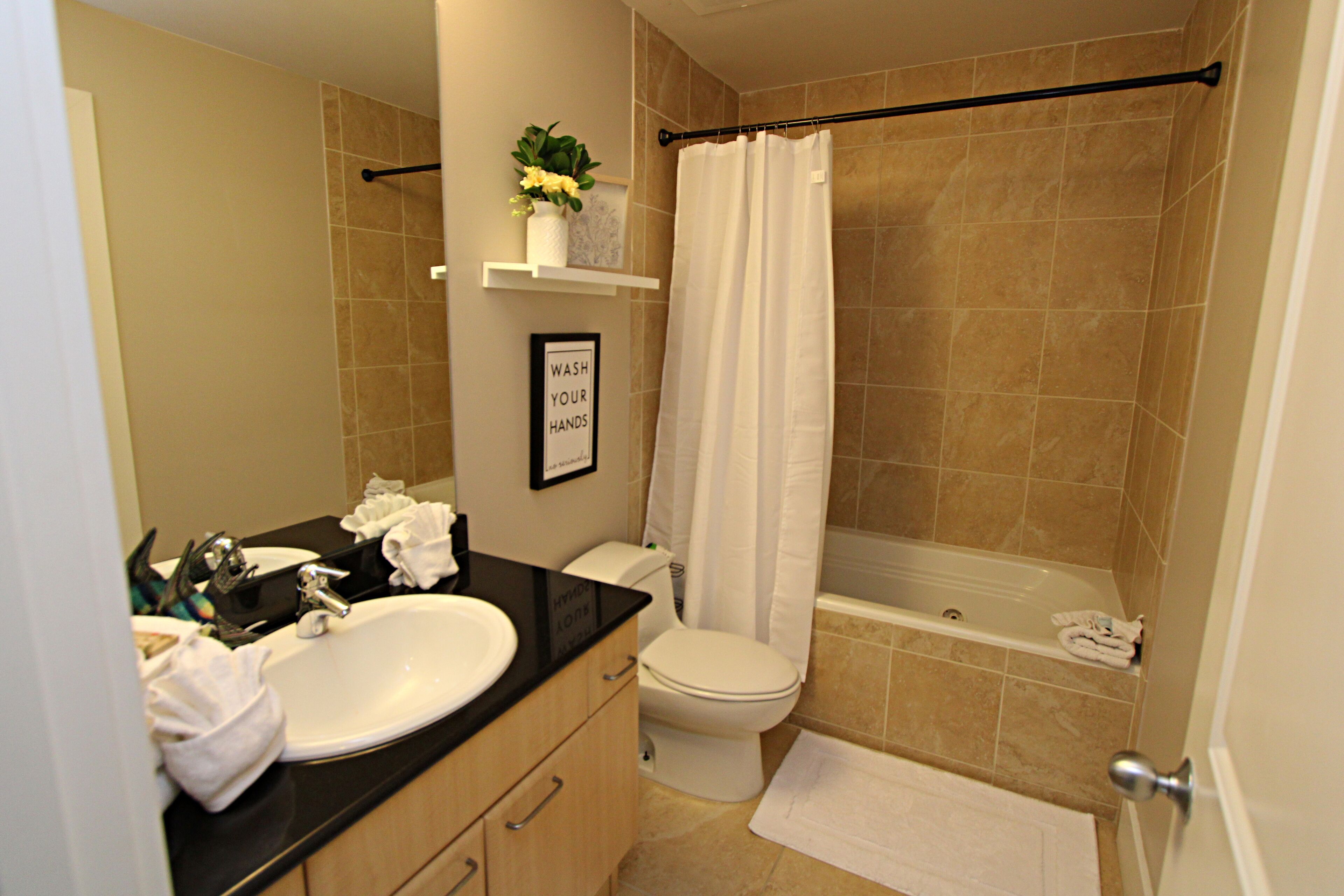A bathroom with a sink, toilet, and bathtub. There is a towel rack and a framed sign on the wall.