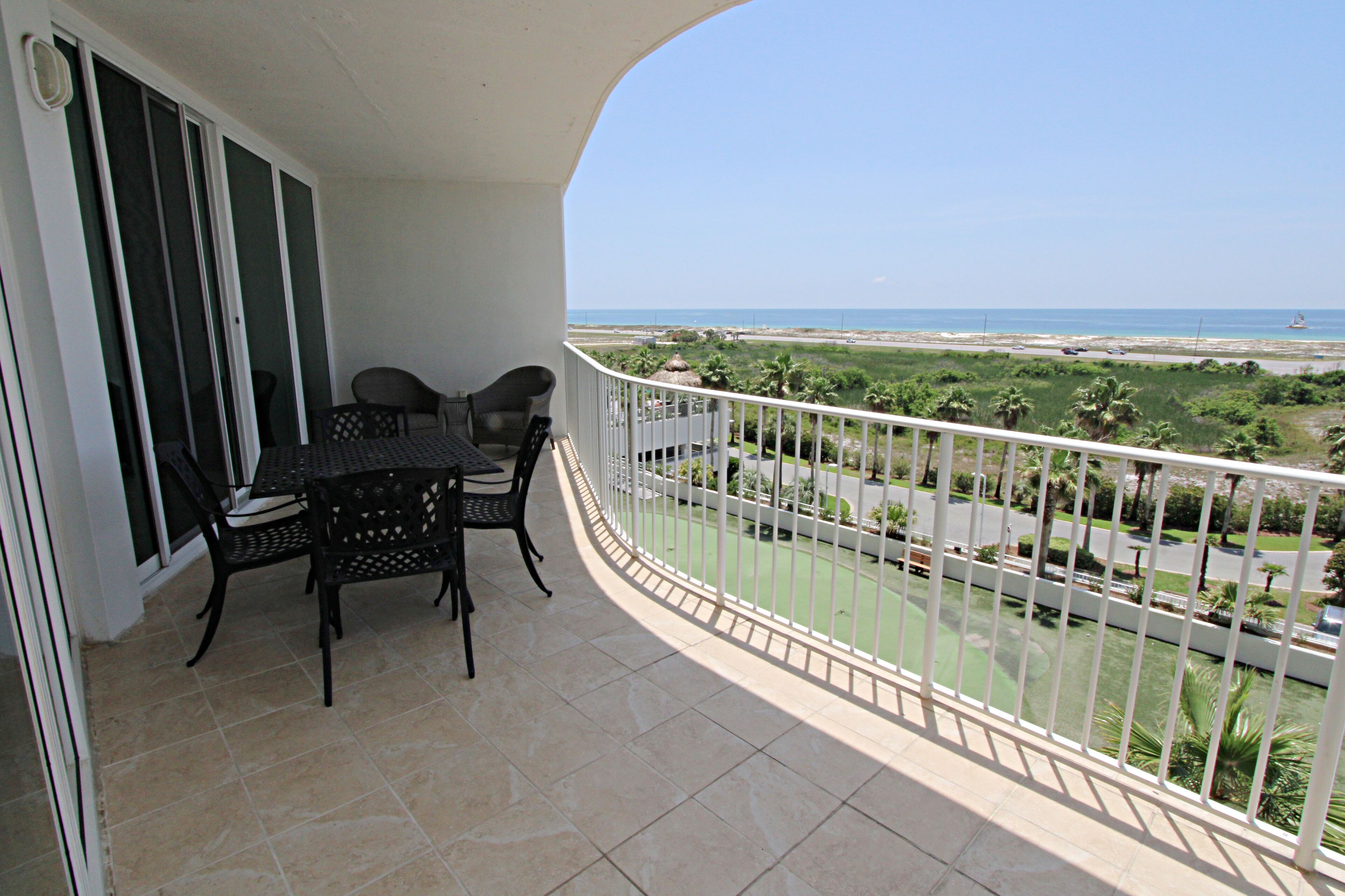 Ein Balkon mit Tisch und Stühlen, der Blick auf Strand und Palmen bietet.