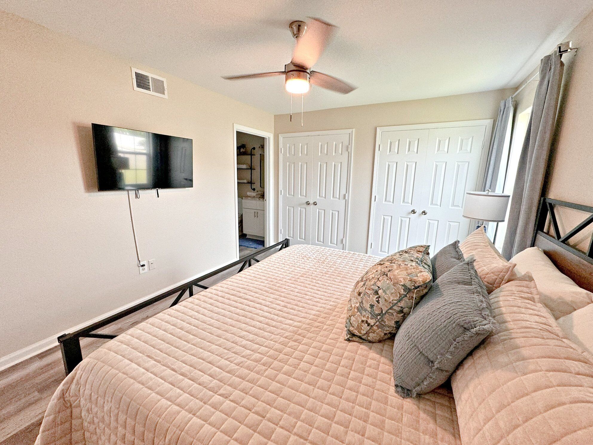 A bedroom with a bed, a ceiling fan, a TV, and a door leading to a bathroom.