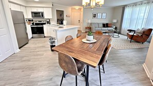 A modern kitchen with white cabinets, stainless steel appliances, and a wooden dining table with chairs. - Colony Club (Gulf Shores)