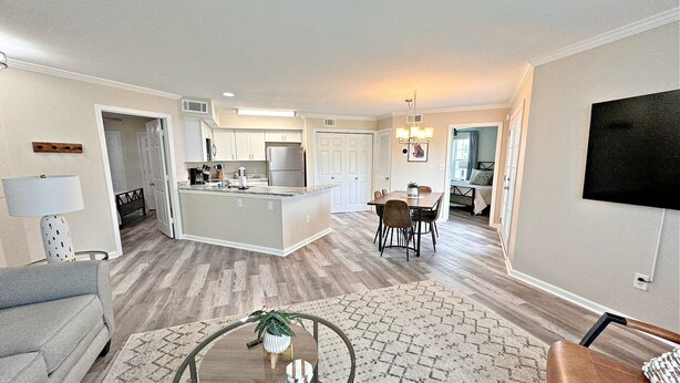 A modern living room with a round glass table, a sofa, and a TV mounted on the wall. - Colony Club (Gulf Shores)