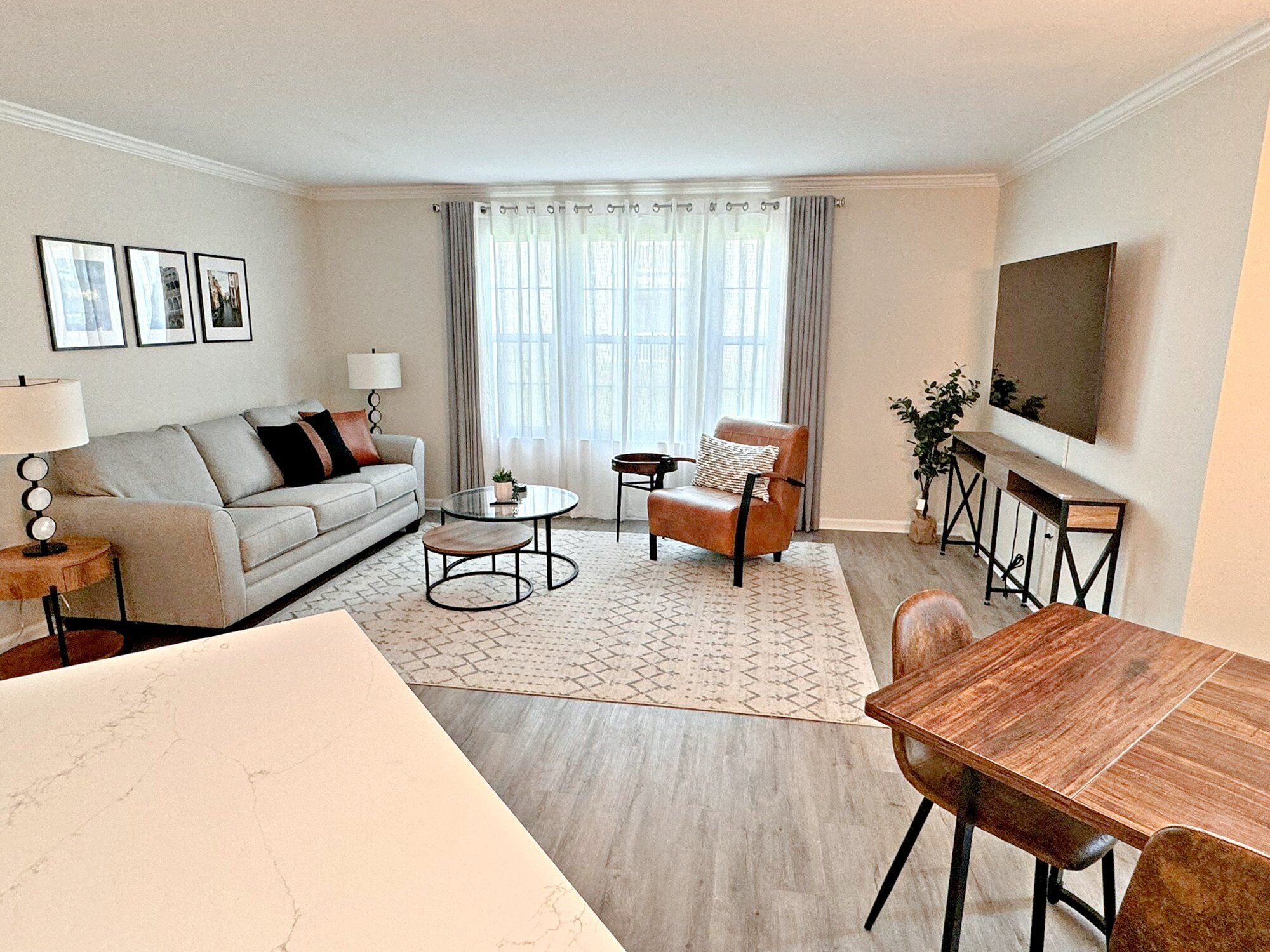 Una sala de estar con sofá, mesa de centro, sillón, mesa de comedor y televisor montado en la pared.