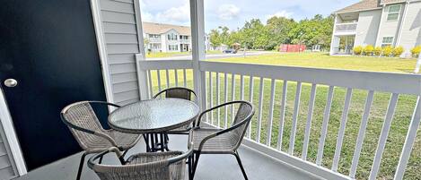 Un patio techado con una mesa y cuatro sillas de mimbre, con vistas a una zona residencial con casas y césped.