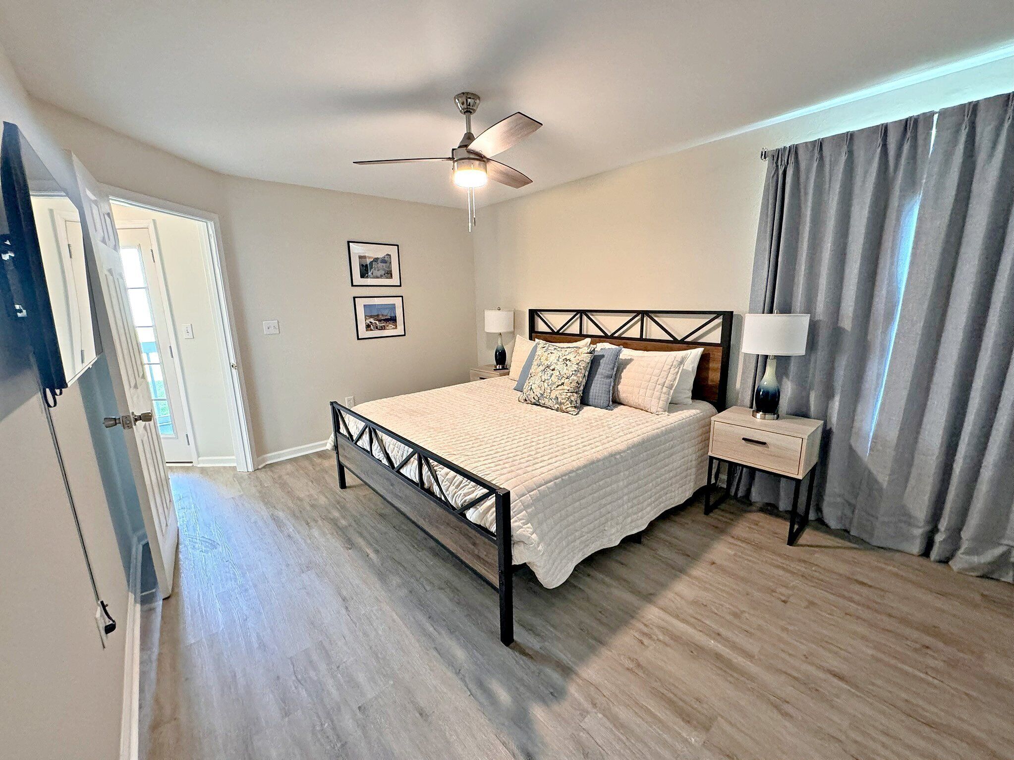 A bedroom with a bed, nightstands, a ceiling fan, and a door.