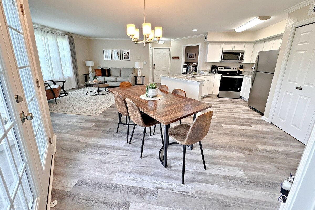 A modern kitchen with white cabinets, stainless steel appliances, and a wooden dining table with chairs.