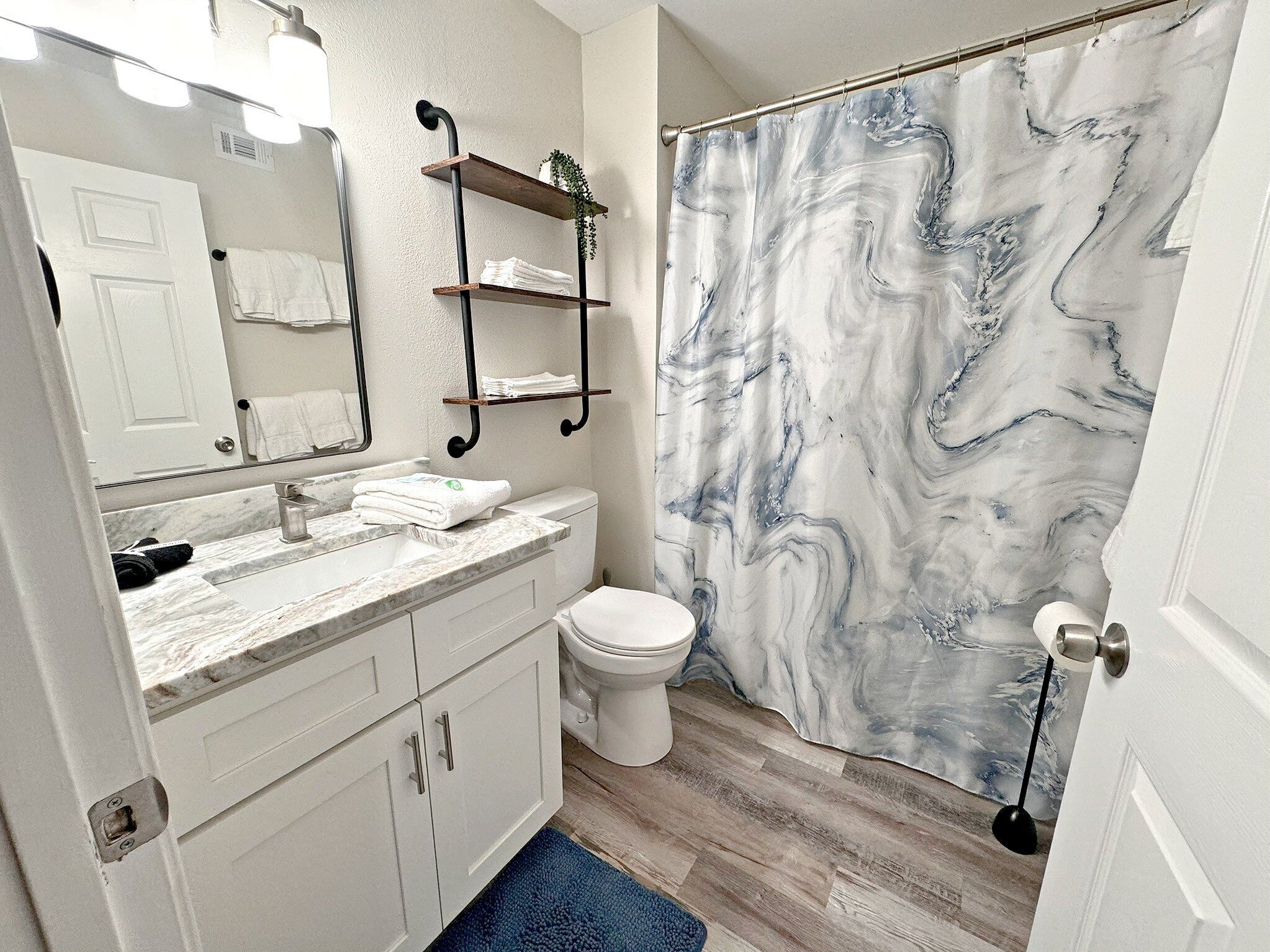 A bathroom with a marble shower curtain, white cabinets, a sink with a mirror, and a toilet.