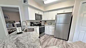 A modern kitchen with white cabinets, a stainless steel refrigerator, a microwave, and a granite countertop. - Colony Club (Gulf Shores)