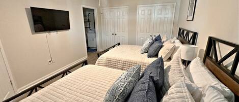 A bedroom with two beds, a ceiling fan, a TV mounted on the wall, and a door leading to a bathroom.