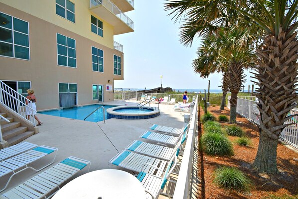 A pool area with lounge chairs, a hot tub, and a building with multiple windows and balconies. - Crystal Shores (Gulf Shores)