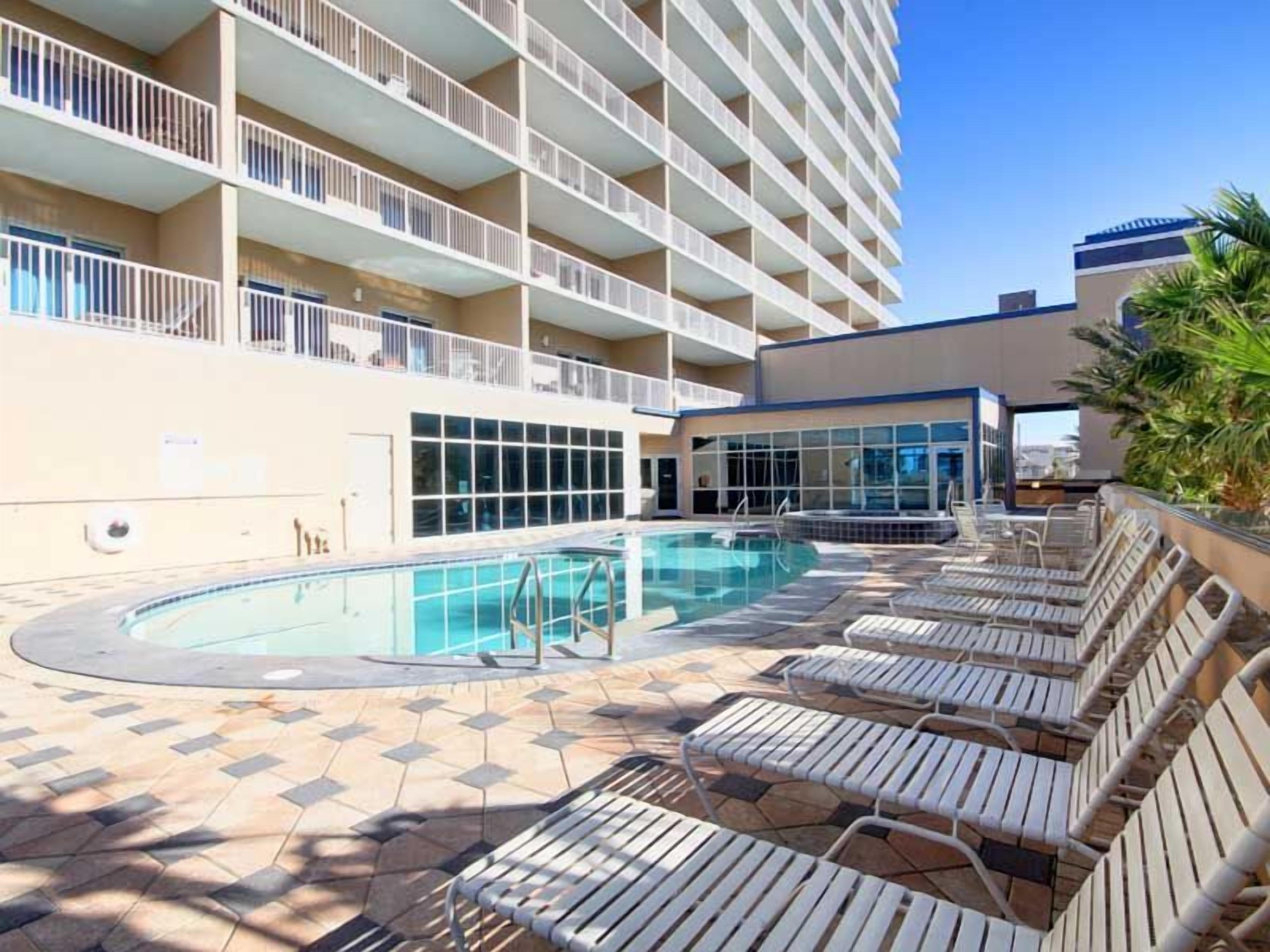 A hotel pool area with a large pool, sun loungers, and a building with balconies.