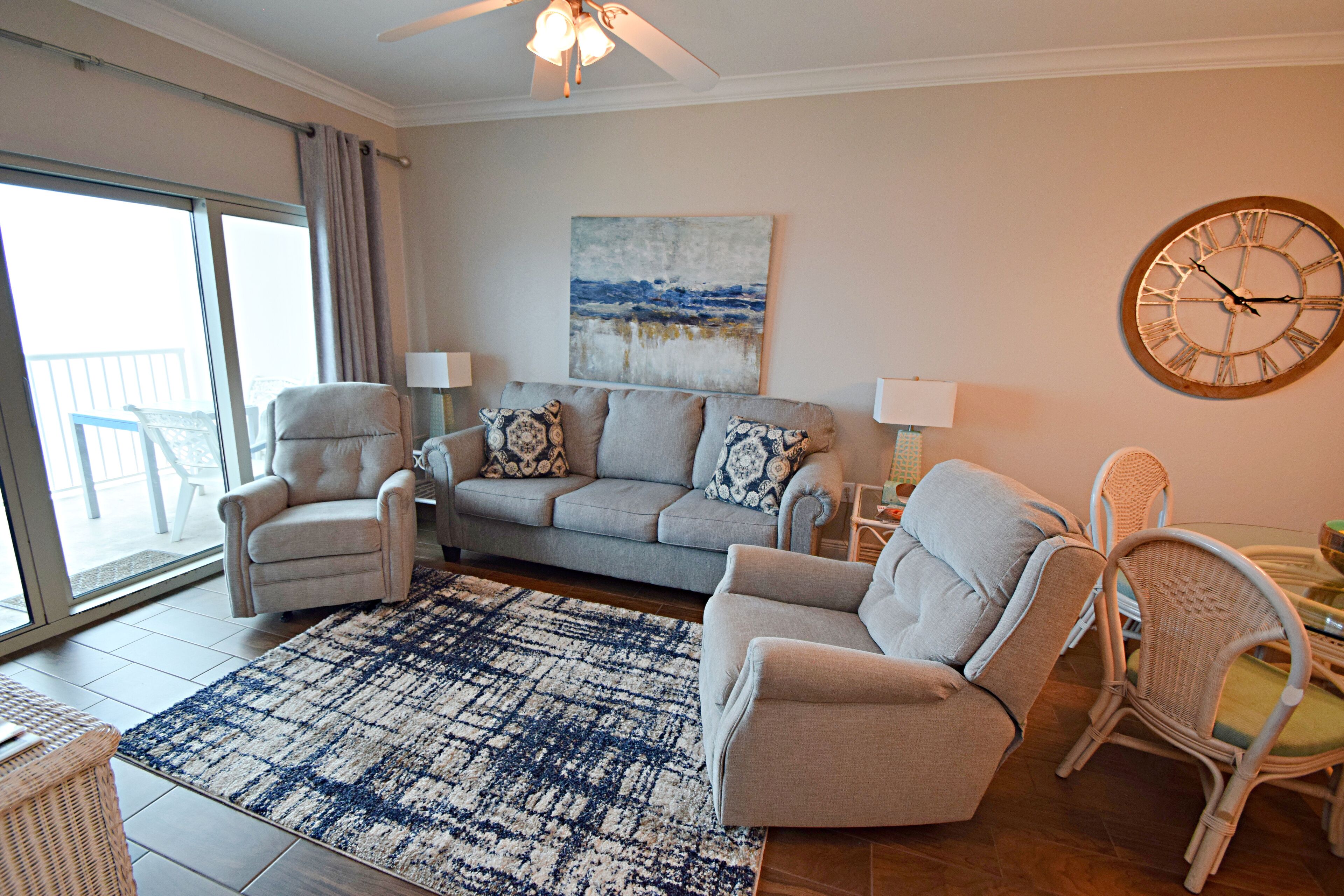 A living room with a sofa, armchairs, a patterned rug, and a wall clock.