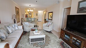Uma sala de estar com sofá, poltronas, mesa de centro, televisão e um armário.
