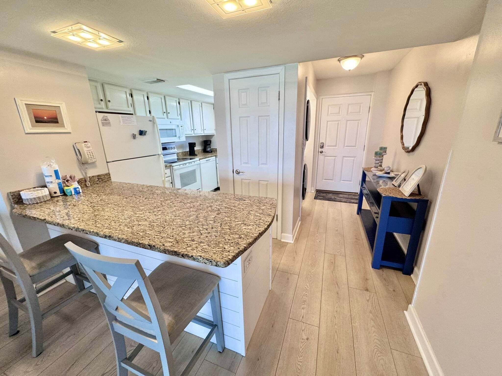 Una cocina con encimera de granito, armarios blancos, refrigerador y microondas.