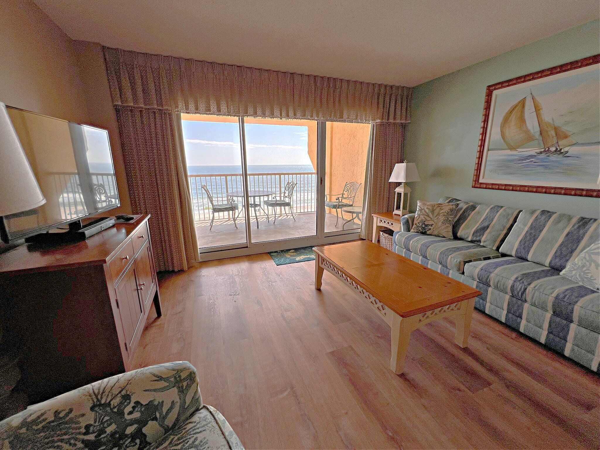A living room with a sofa, a coffee table, a TV, and a balcony with a view of the sea.
