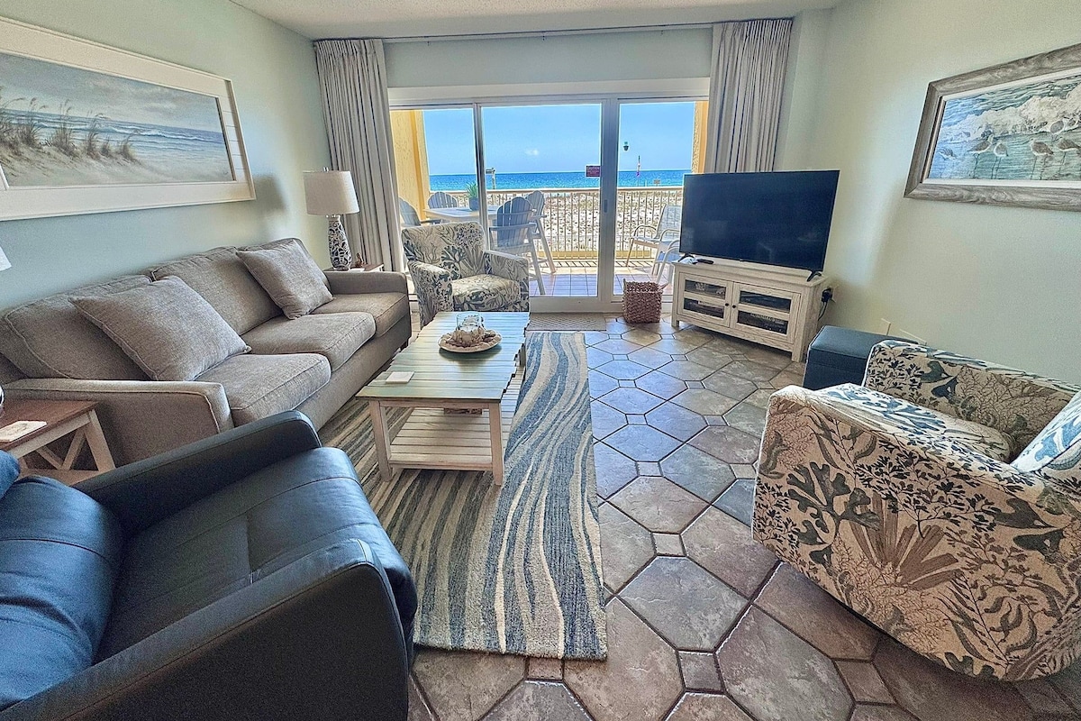 Un salon comprenant un canapé, un fauteuil, une table basse et un téléviseur, avec vue sur la mer grâce à une porte vitrée.