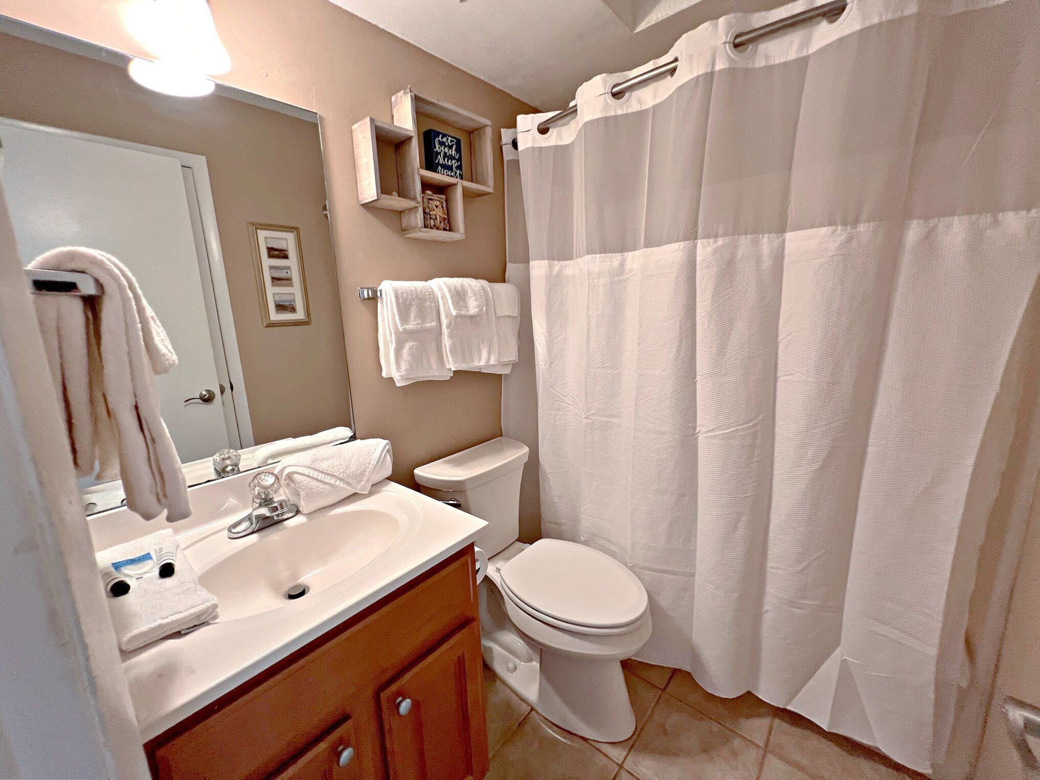 Un baño con lavamanos, espejo, inodoro y cortina de ducha.