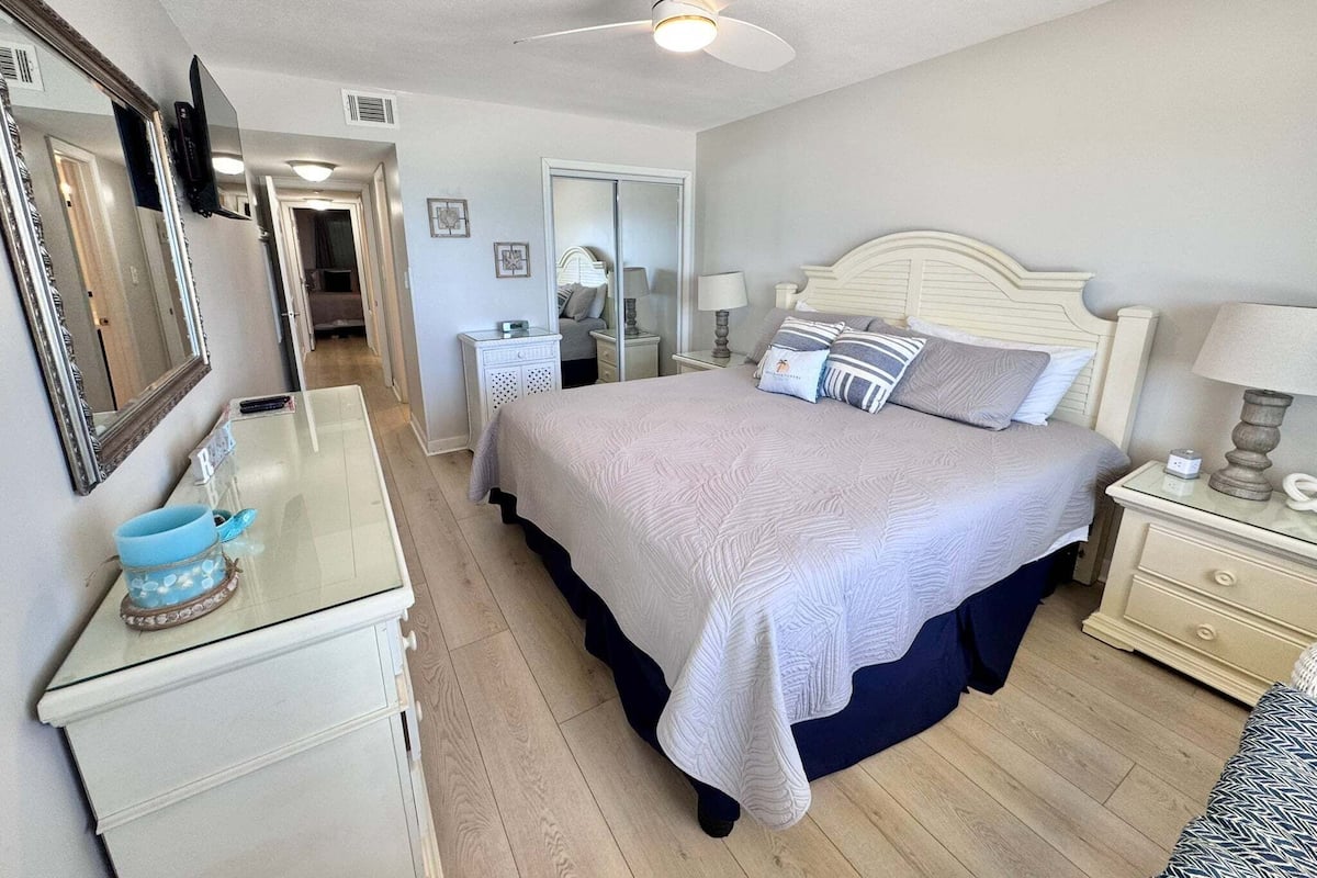 Un dormitorio con cama, mesitas de noche, cómoda, ventilador de techo y espejo.