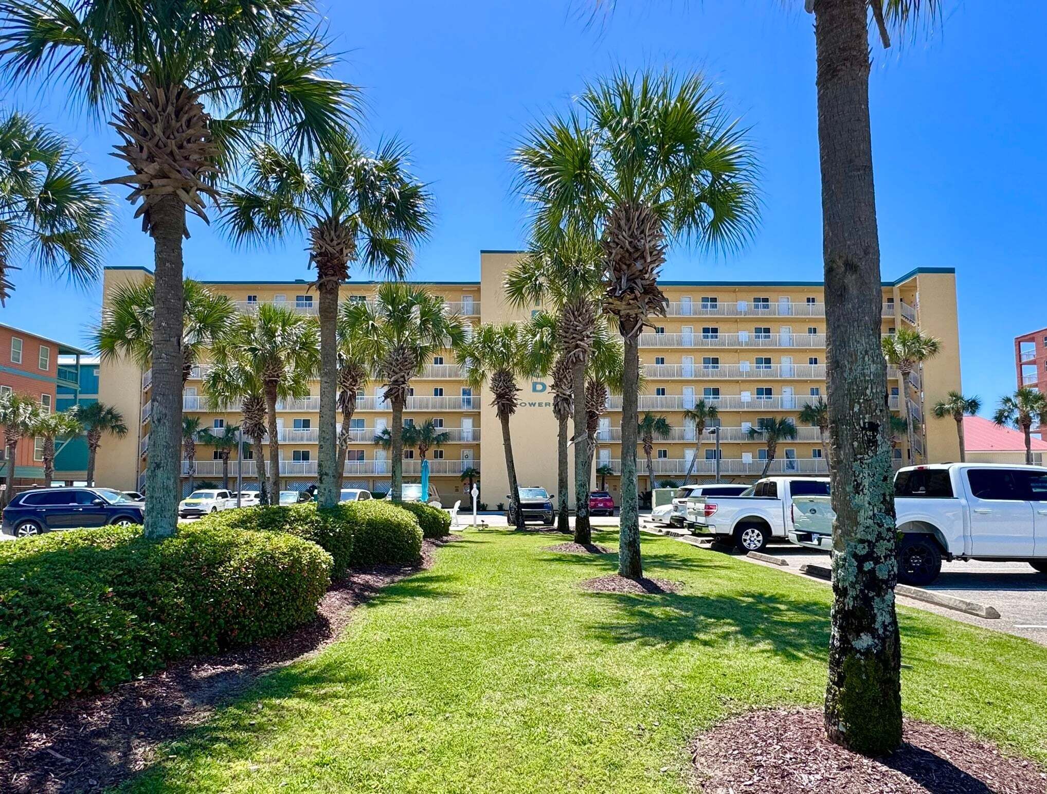 A hotel with a central courtyard, palm trees, and a parking lot with several vehicles.