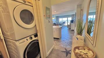 A laundry area with stacked washers and dryers, a kitchen with a central island, and a view to a balcony.
