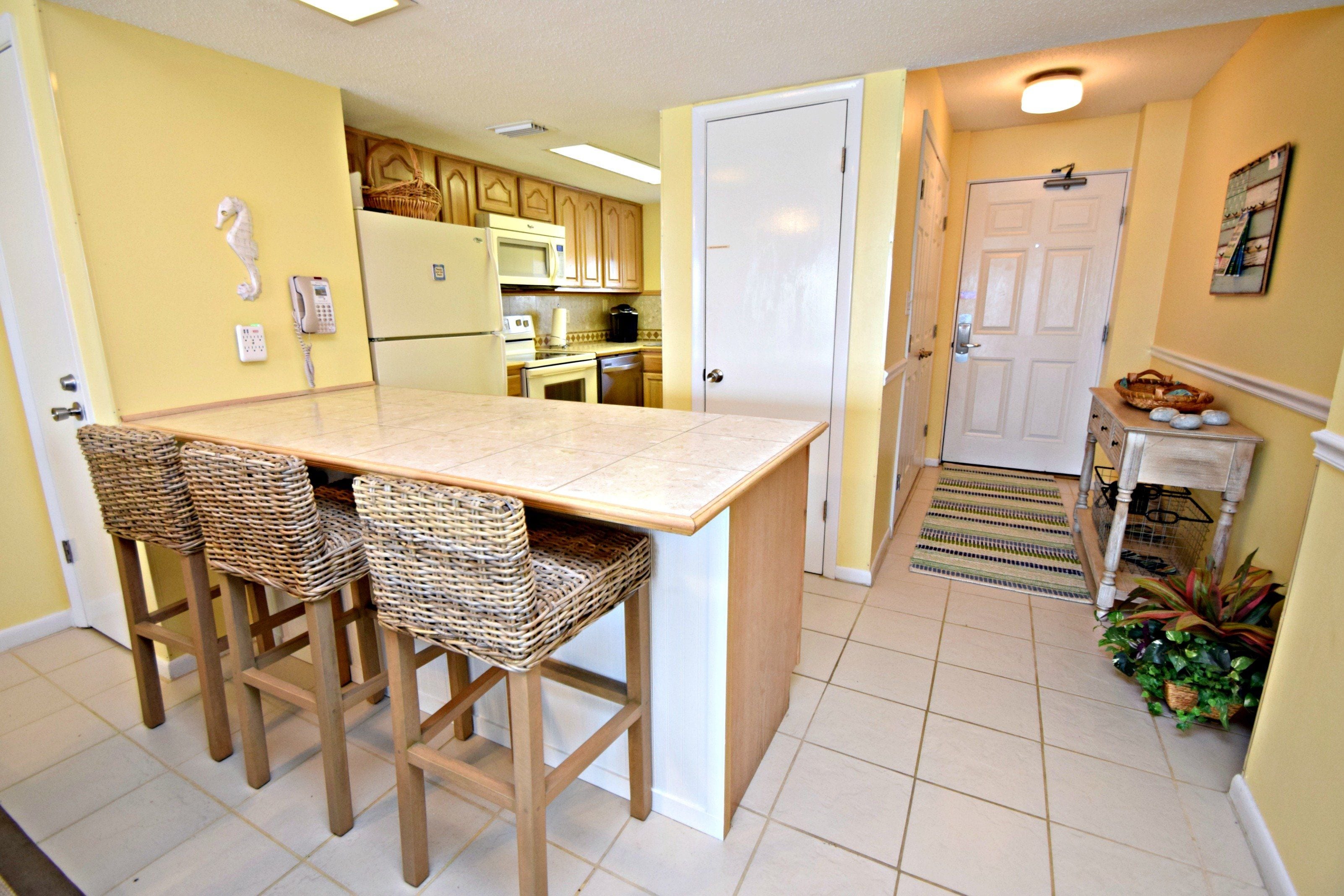 A kitchen with a central island, bar stools, a refrigerator, a microwave, and a stove.