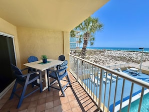 A balcony with a table and chairs, a pool, and a beach view. - Driftwood Towers (Gulf Shores)
