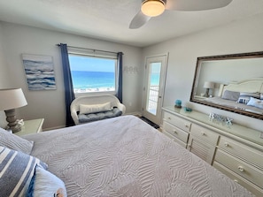 A bedroom with a bed, dresser, and a window with a view of the beach.